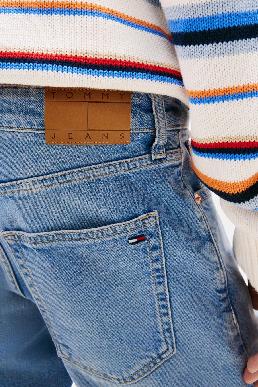 Mid blauwe denim jeansshort van TOMMY JEANS, met leren logopatch en vlagdetail op de achterzak, gedragen met een gestreepte trui.