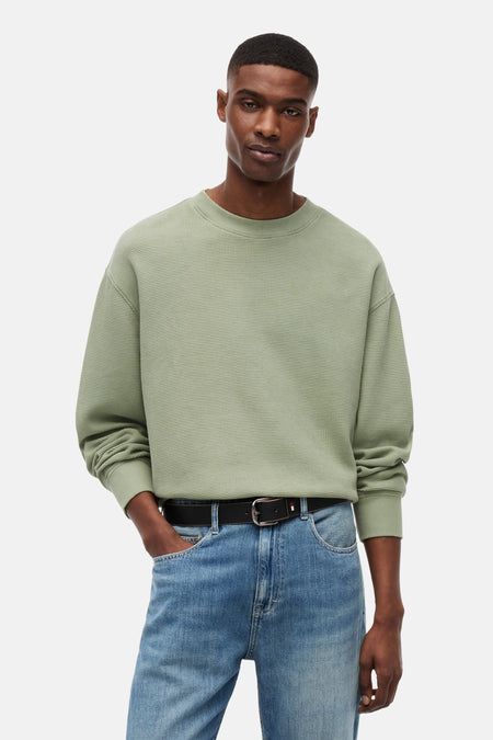 Pull vert avec col rond de TOMMY JEANS avec texture gaufrée, logo sur l'ourlet et porté par un homme.