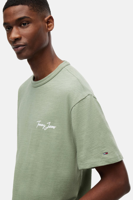 Groen T-shirt met korte mouwen van TOMMY JEANS, met gemêleerde stof, wit scriptlogo en vlaglogo, gedragen door een model.