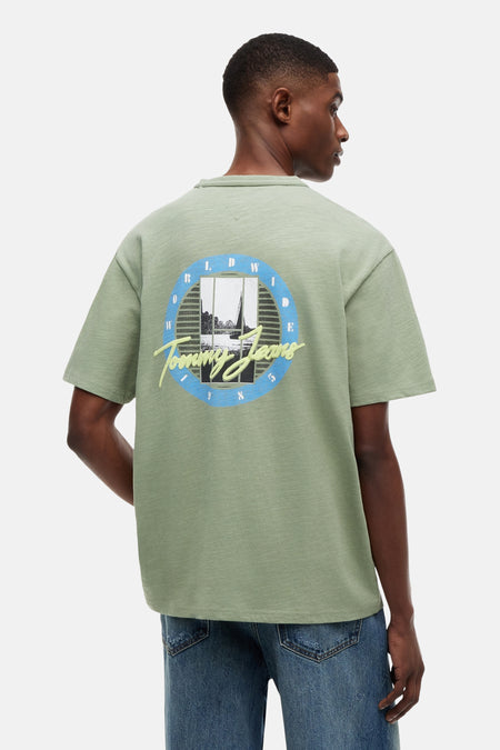 T-shirt vert à manches courtes TOMMY JEANS, dos, avec imprimé paysage aquatique rond et "Tommy Jeans" dans le dos, combiné avec un jean.