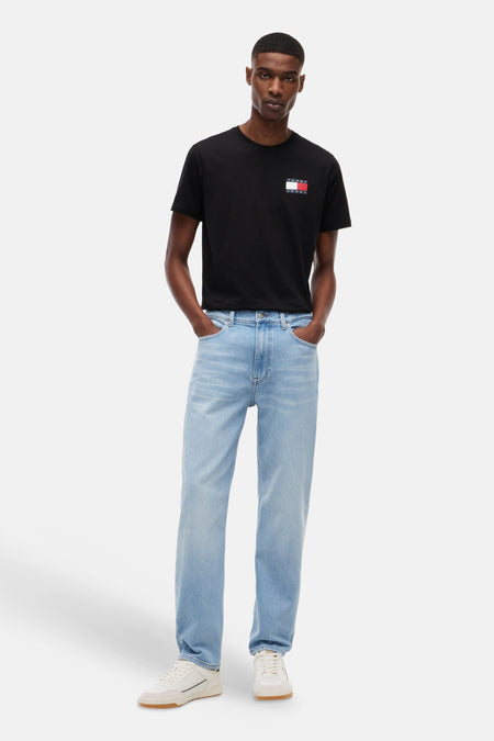 Lichtblauwe tapered jeans van TOMMY JEANS, gedragen door een man met een zwart T-shirt en witte sneakers.