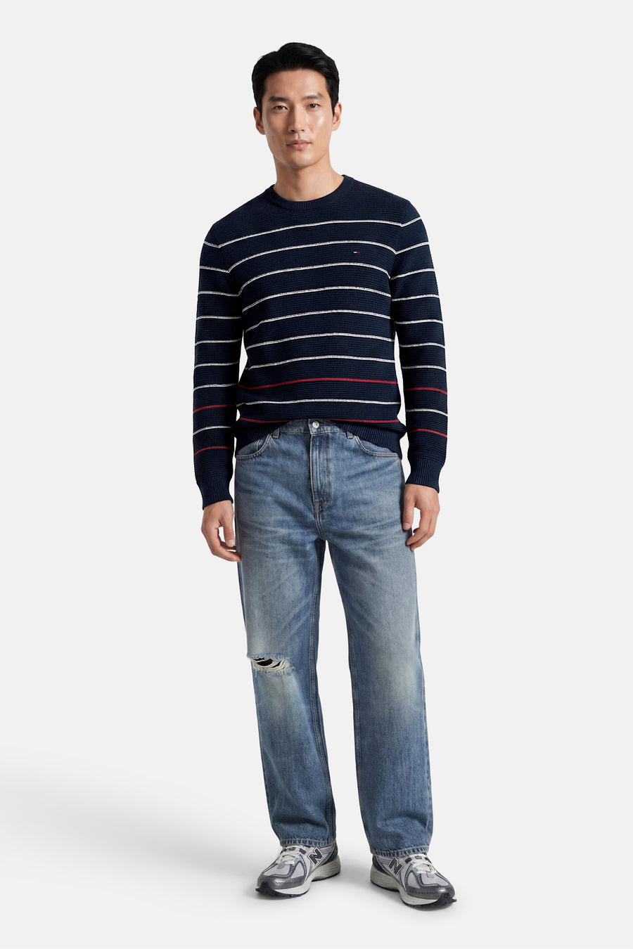 Blauwe ronde hals trui met witte en rode strepen van TOMMY JEANS, gedragen met grijze jeans en sneakers, front view