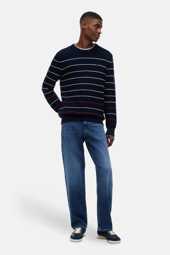 Blauwe trui met ronde hals van TOMMY JEANS, met witte en rode strepen, ribgebreid, gedragen door een man met jeans en sneakers.