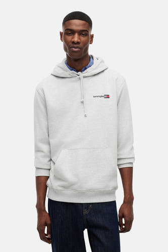 Grijze sweater van TOMMY JEANS in hoodie-stijl met klein borstlogo, gedragen over een blauw geruit overhemd en donkere jeans.