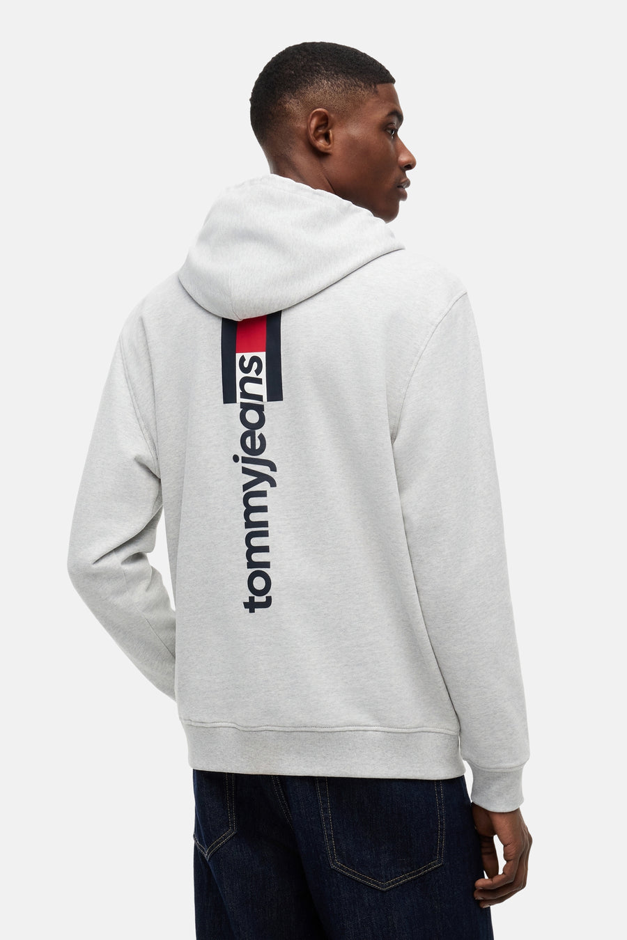 Grijze sweater met capuchon van TOMMY JEANS, met verticale rood-navy streep en 'tommyjeans' logo op de rug.