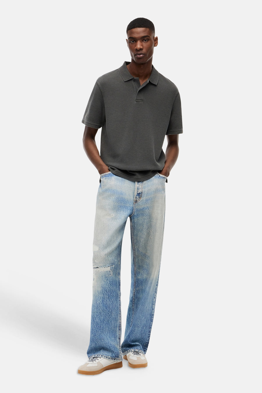 Zwart polo met fijn geruit patroon van TOMMY JEANS, gedragen met lichtblauwe versleten jeans en beige sneakers, front view.