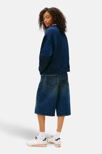 Blauwe sweater van TOMMY JEANS, gedragen met denim bermuda en witte sokken met sneakers.