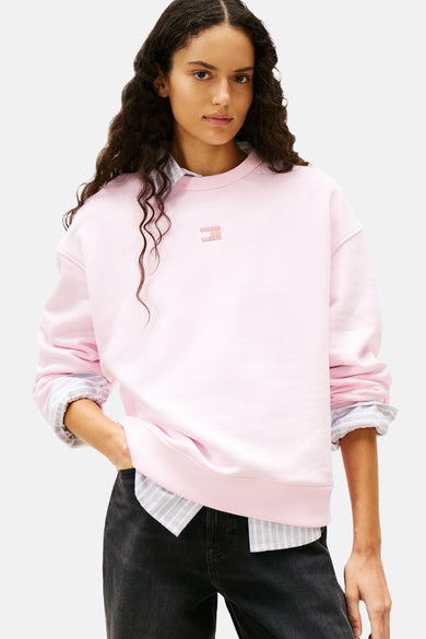 Roze sweater met ronde hals van TOMMY JEANS, gedragen over een gestreept overhemd en gecombineerd met donkere jeans.