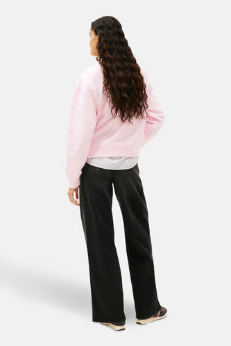 Roze sweater van TOMMY JEANS, met lange mouwen en een ronde hals, gedragen met een gestreept overhemd en zwarte jeans.