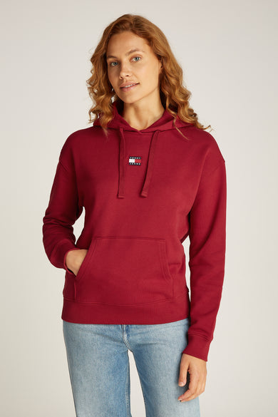 Rode sweater met kap van TOMMY JEANS, met buidelzak en lichtblauwe jeans.
