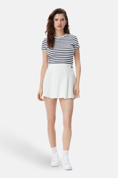 T-shirt bleu rayé à manches courtes de TOMMY JEANS, porté avec une jupe blanche et des baskets blanches.