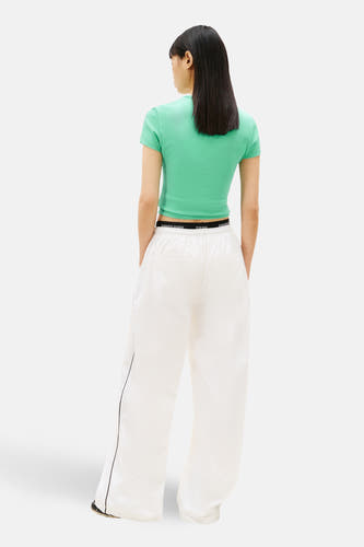 Groen T-shirt met korte mouwen van Tommy Jeans, gezien van achteren met een zichtbare tailleband en een witte broek.
