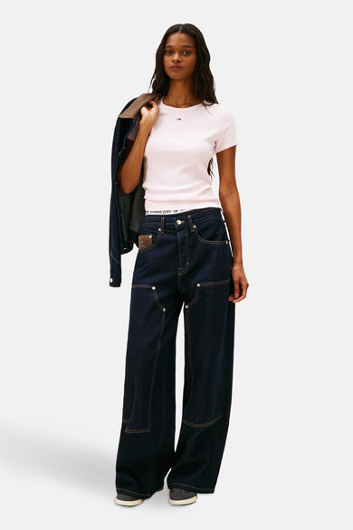 T-shirt rose à manches courtes de TOMMY JEANS, avec une veste en denim sur l'épaule et des jeans bleu marine.