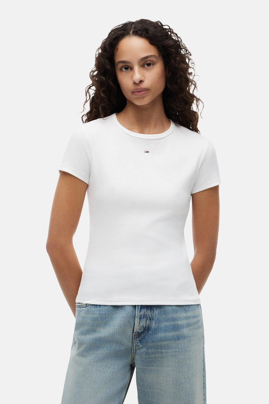 Wit geribbelde T-shirt van TOMMY JEANS met klein logo op de borst, gedragen door een model met een lichte spijkerbroek.