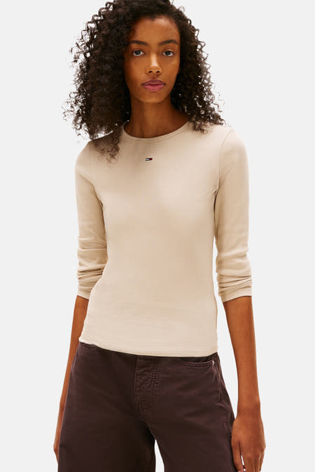 Beige T-shirt met lange mouwen van TOMMY JEANS, geribbelde textuur, gedragen met een bruine broek.
