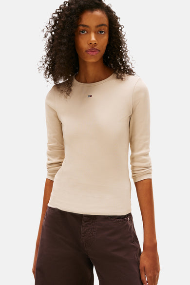 Beige T-shirt met lange mouwen van TOMMY JEANS, geribbelde textuur, gedragen met een bruine broek.
