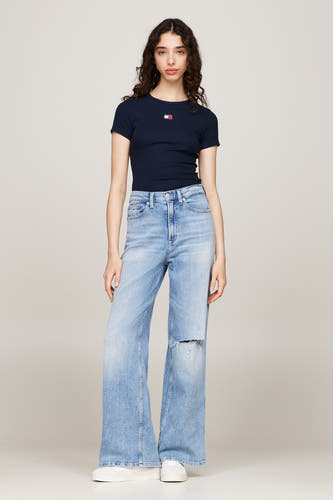 Blauw T-shirt met korte mouwen van TOMMY JEANS, gedragen met wijde, lichtblauwe jeans met scheuren en witte sneakers.
