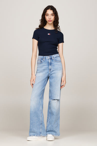 Blauw T-shirt met korte mouwen van TOMMY JEANS, gedragen met wijde, lichtblauwe jeans met scheuren en witte sneakers.
