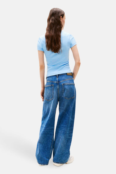 T-shirt bleu à manches courtes de TOMMY JEANS, associé à des jeans décontractés longs et à des baskets blanches.