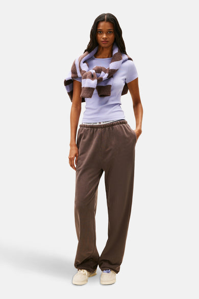Paars T-shirt met korte mouwen van Tommy Jeans, met een gestreepte trui om de schouders en bruine joggingbroek.
