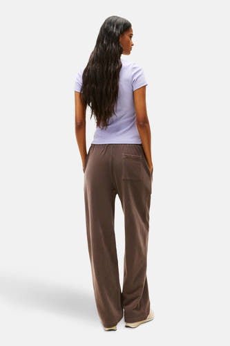 Paars T-shirt met korte mouwen van TOMMY JEANS, met lange bruine joggingbroek en schoenen op de achterkant.
