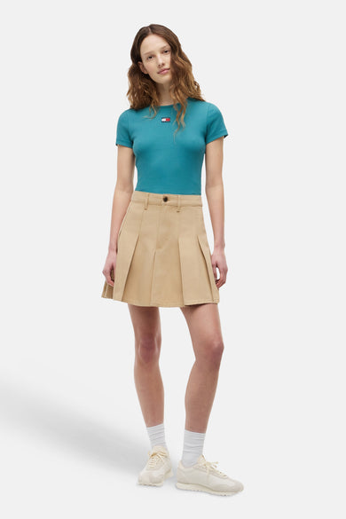 Petrolgroen geribbeld T-shirt van TOMMY JEANS met klein logo en korte mouwen, gedragen door een model met een beige minirok en witte sneakers.