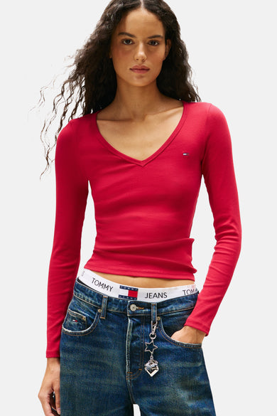 Roze T-shirt met lange mouwen van TOMMY JEANS, met een V-hals en gedragen met een jeans met een witte band.
