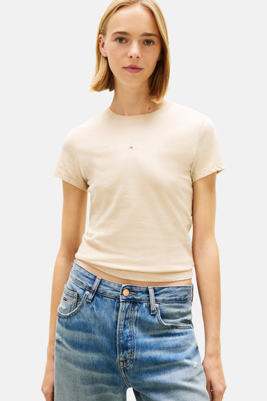 Beige T-shirt van TOMMY JEANS, met korte mouwen en subtiel logo op de borst, gedragen met jeans.
