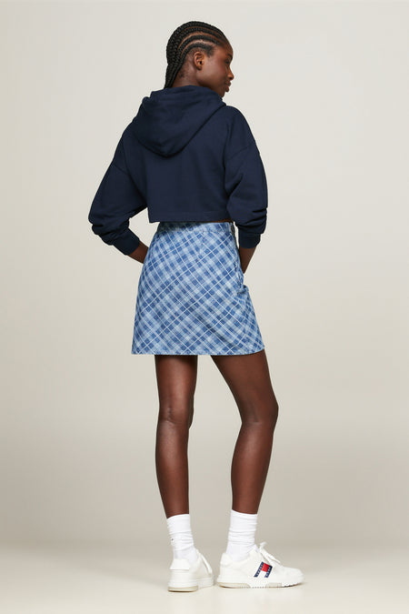 Blauwe korte rok van TOMMY JEANS met ruitpatroon, van achteren gezien op een model met een donkerblauwe hoodie en witte sneakers.