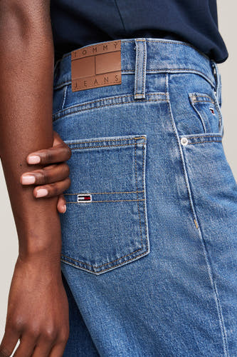 Jean mom bleu de denim par TOMMY JEANS, avec une étiquette en cuir et des accents rouges sur le dos.