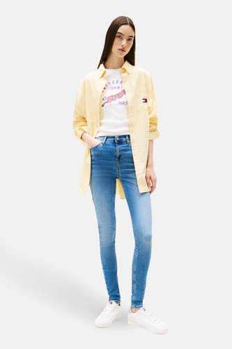 Mid blue skinny jeans denim van Tommy Jeans, gedragen met een geel overhemd en een wit T-shirt.
