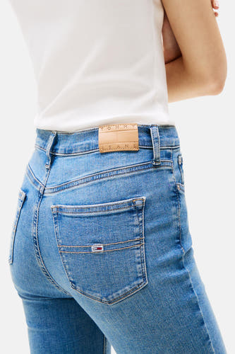 Blauw skinny jeans van TOMMY JEANS, met een klein merklogo op de achterzak, gedragen met een wit shirt.
