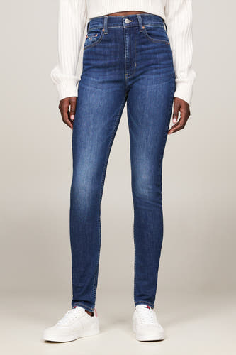 Donkerblauwe skinny jeans van TOMMY JEANS, met een witte trui en witte sneakers.
