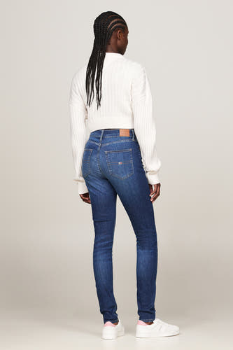 Donkerblauwe skinny jeans van TOMMY JEANS, met een witte trui en witte sneakers.
