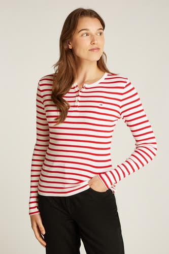 Rood-wit gestreepte longsleeve van TOMMY JEANS, met knoopjes bij de hals en gedragen met een zwarte broek.
