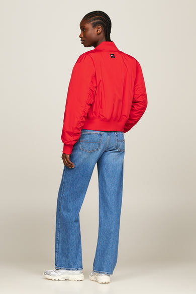 Rode jas van TOMMY JEANS, met lange mouwen, gedragen met wijde jeans en witte sneakers.
