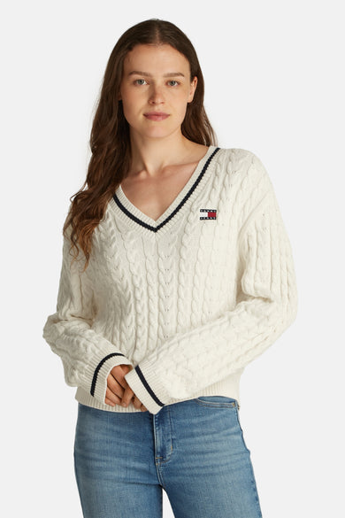 Witte V-halstrui van TOMMY JEANS, met kabelpatroon en blauwe randen, gedragen met een blauwe jeans.
