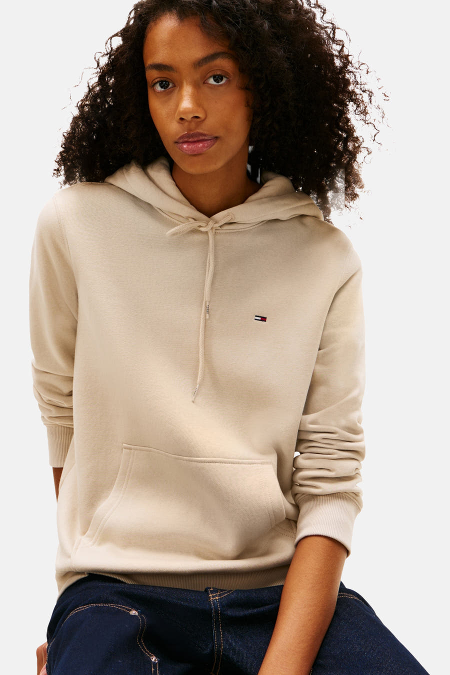 Beige sweater van TOMMY JEANS, met capuchon, lange mouwen en donkerblauwe jeans.
