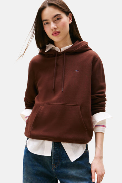 Bruine sweater met ronde hals van TOMMY JEANS, met een capuchon, gecombineerd met een wit overhemd en een blauwe jeans.

