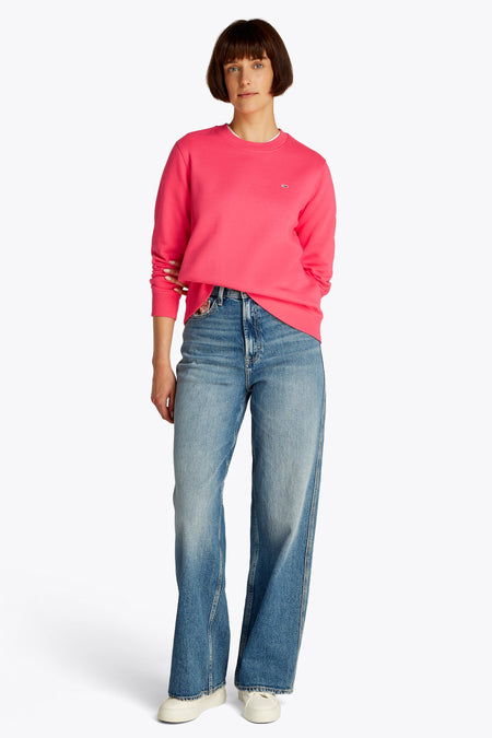 Roze sweater van TOMMY JEANS, gecombineerd met een jeans en crèmekleurige schoenen.