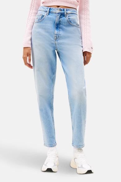 Mom jeans van lichtblauw denim van TOMMY JEANS, gecombineerd met een roze trui en witte sneakers.
