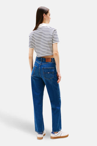 Jean bleu marine droit de TOMMY JEANS, avec étiquette en cuir marron et associé à une chemise rayée et des baskets.