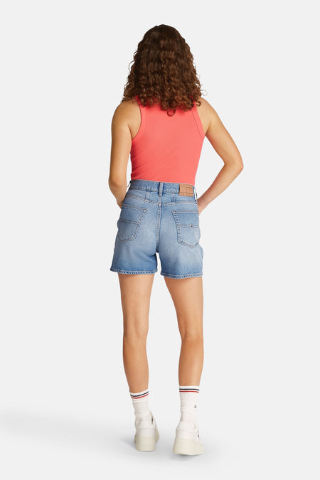 Korte lichtblauwe denim van Tommy Jeans, gezien van achteren, gecombineerd met een roze top en witte sokken met strepen.
