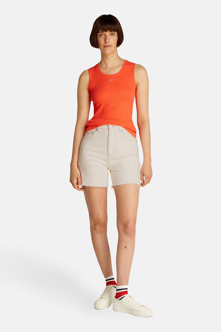 Short de denim blanc de TOMMY JEANS, porté avec un haut orange et des baskets blanches avec des chaussettes rayées.
