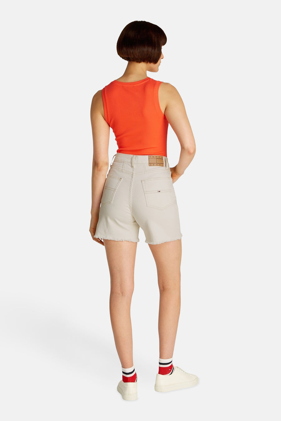 Short en denim blanc de Tommy Jeans, avec des bords froncés et associé à un haut orange.