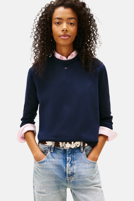 Blauwe trui met ronde hals van TOMMY JEANS, gecombineerd met een roze blouse en een riem met koeienprint.
