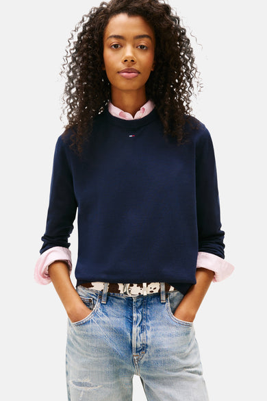 Blauwe trui met ronde hals van TOMMY JEANS, gecombineerd met een roze blouse en een riem met koeienprint.
