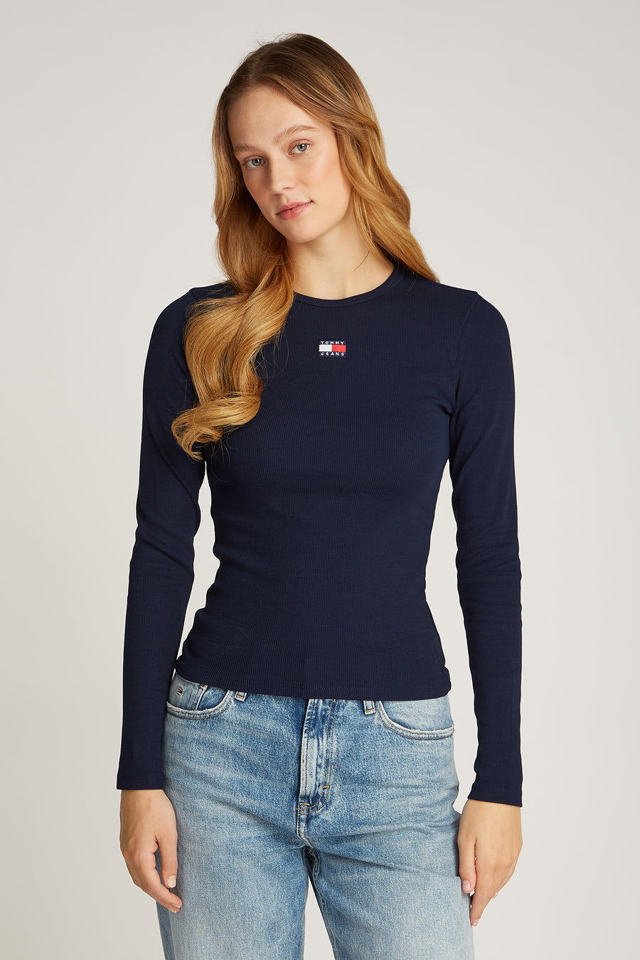 Donkerblauwe longsleeve T-shirt van TOMMY JEANS, met een ribgebreide textuur en een logo op de borst, gedragen met een blauwe spijkerbroek.
