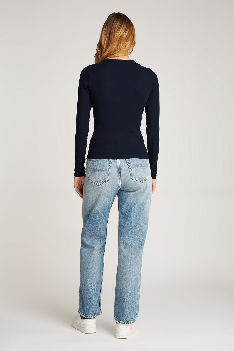 Blauw shirt met lange mouwen van TOMMY JEANS, gedragen met lichtblauwe jeans en witte sneakers.
