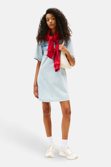 Lichtblauwe denim jurk met korte mouwen van TOMMY JEANS, met rode trui en witte tas.